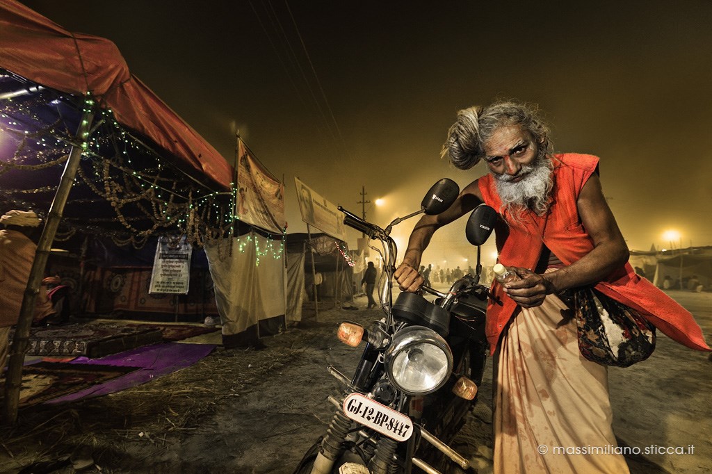 A Naga Sadhu with his motorbike, near a tent in Kumbh Mela